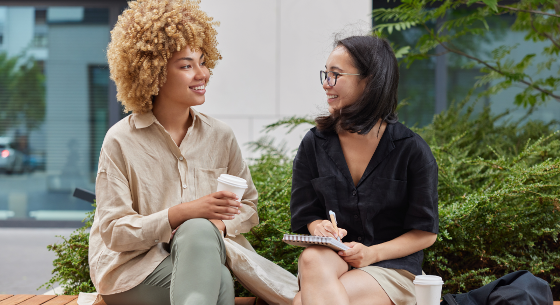 two women sitting side by side outside