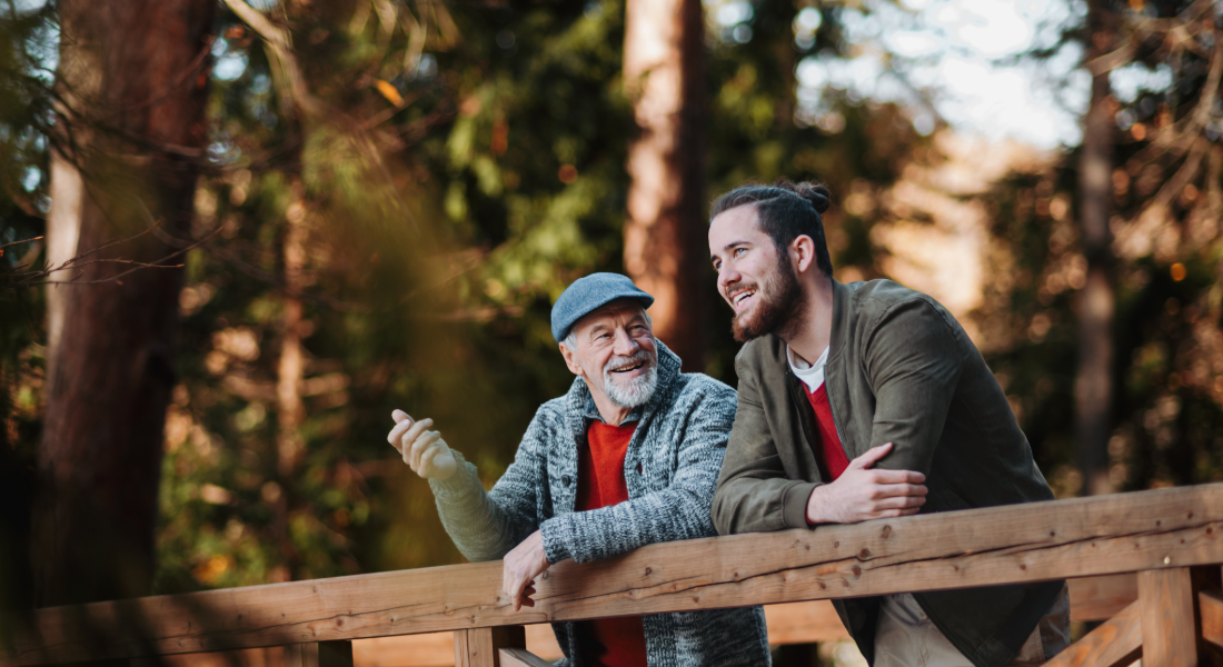 Two men, outdoors, leaning against a railing, talking