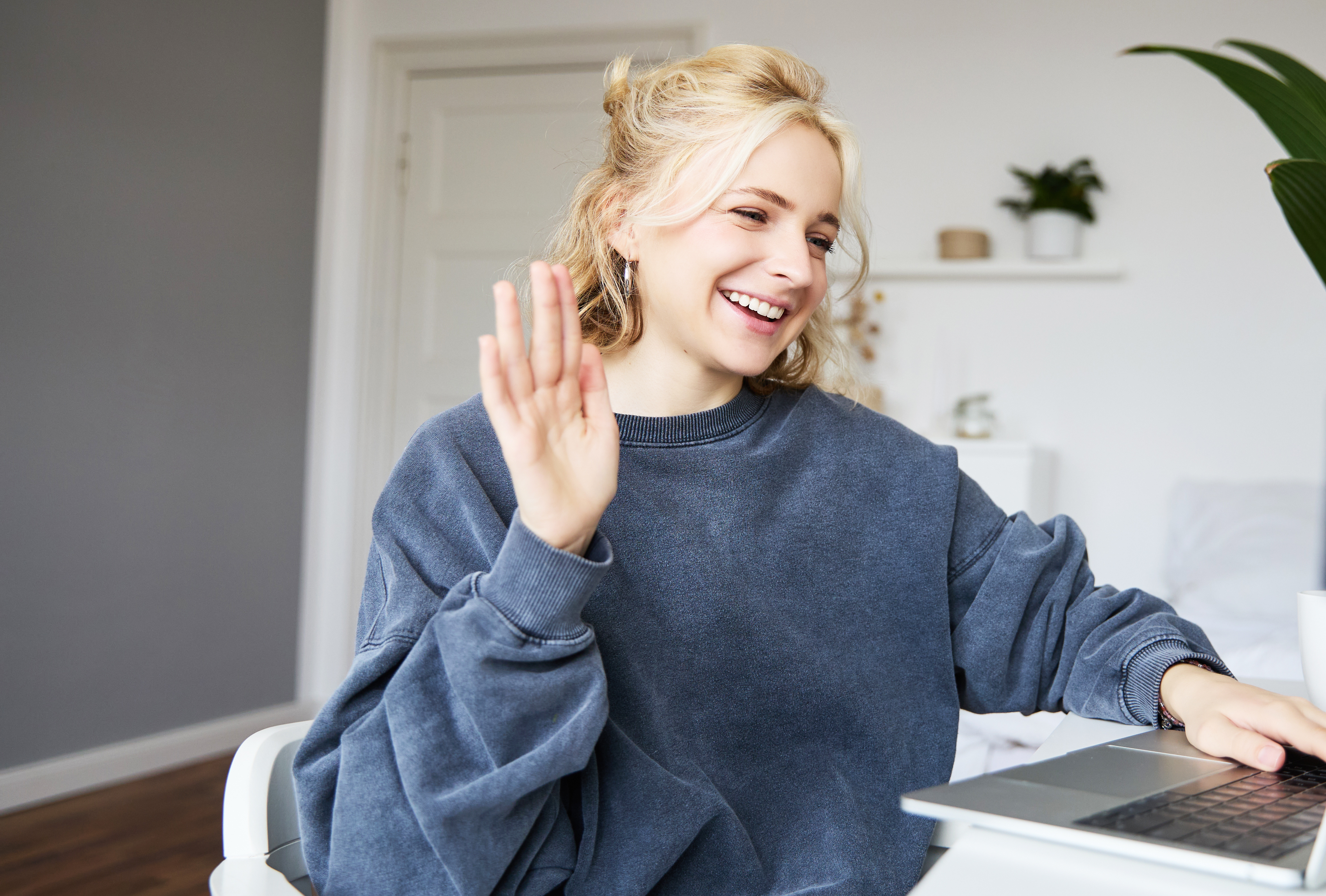 young woman waves at camera on computer
